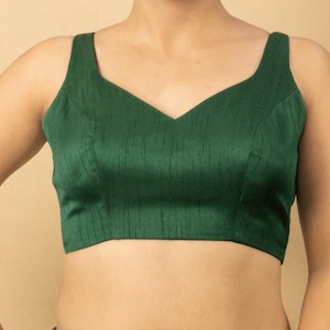 Puede incluir: Un top sin mangas verde oscuro con cuello en V. El top está hecho de una tela suave y texturizada. La prenda tiene una silueta ajustada y está diseñada para ser usada sola o en capas.