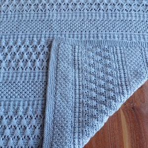 May include: A light blue knitted baby blanket with a delicate lace pattern. The blanket is folded in half, showing the different stitch patterns.