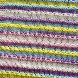 以下が含まれることがあります： パステルカラーの横縞模様のニット生地のクローズアップ。縞模様は白、ピンク、黄色、水色、紫を交互に繰り返しています。ニットの質感がはっきりと見え、わずかに浮き出た模様があります。