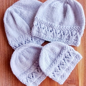 May include: Four light blue knitted baby hats. The hats are arranged on a wooden surface. Two hats have a decorative openwork pattern near the brim. The hats are made of soft yarn.
