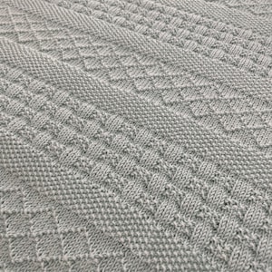 May include: A close-up of a light blue knitted blanket with a diamond pattern.