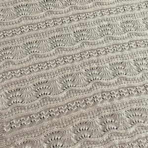 Könnte beinhalten: Nahaufnahme einer beige gehäkelten Decke mit einem sich wiederholenden Muster aus kleinen Kreisen und Bögen.