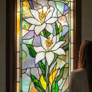 Puede incluir: Una ventana de vitrales con un diseño floral que presenta dos lirios blancos con centros amarillos y hojas verdes. El fondo es una mezcla de morado, azul y amarillo.
