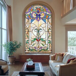 Puede incluir: Una ventana de vitrales con un diseño floral en tonos azules, verdes, amarillos y morados. La ventana es arqueada y está empotrada en una pared blanca. La ventana está en una sala de estar con un sofá y una mesa de café.