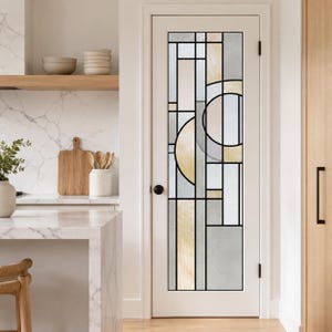 Peut inclure: Une porte intérieure blanche dotée d'un grand panneau vitré rectangulaire au motif géométrique en vitrail. Le design se compose de lignes de plomb noires formant des rectangles, des carrés et des cercles, remplis de verre texturé crème, beige et gris.
