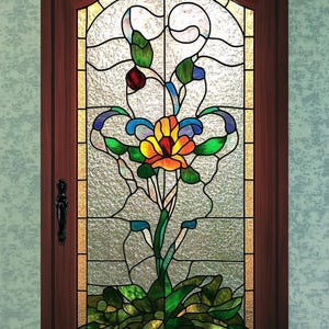 Puede incluir: Una ventana de vitral con un diseño floral. La ventana presenta una gran flor naranja con hojas verdes y detalles azules. La ventana está enmarcada en madera.