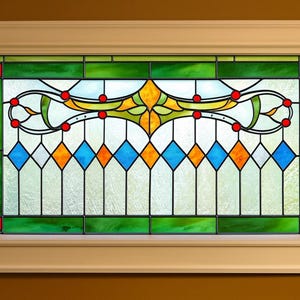 May include: Stained glass window in a cream-coloured wooden frame. The window features a design with green, blue, orange, and yellow glass. The design includes diamond shapes, curved lines, and red accents, creating a decorative and colourful piece.