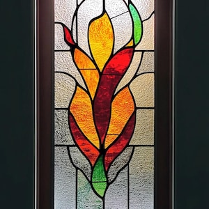 Puede incluir: Una ventana de vitrales con un diseño de flor estilizado con piezas de vidrio rojo, naranja y verde.