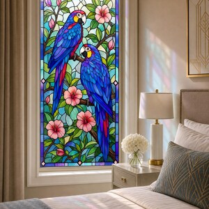 Puede incluir: Un panel de ventana de vidriera rectangular que presenta dos vibrantes guacamayos azules y rojos posados en ramas entre follaje verde y flores de hibisco rosadas. El diseño se compone de numerosos segmentos de vidrio con bordes de plomo.