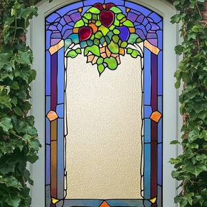 Puede incluir: Una ventana de vitrales con un diseño colorido de un árbol con frutas. La ventana está enmarcada en blanco y colocada en una pared de ladrillo.