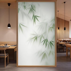 Puede incluir: Panel decorativo con una imagen suave y borrosa de hojas de bambú en tonos verdes sobre un fondo blanco. Las hojas están delicadamente representadas, creando una sensación de tranquilidad. El panel está enmarcado en madera marrón claro.