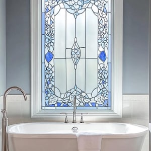 May include: A white bathtub with a white towel on the side. The bathtub is in front of a window with a stained glass design featuring blue and white floral patterns.