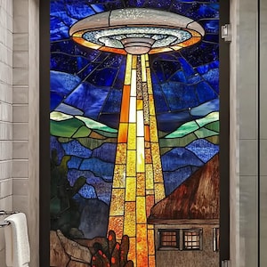 Puede incluir: Una ventana de vitral que representa un platillo volante con un rayo de luz que brilla sobre un paisaje desértico con una pequeña casa y plantas de cactus.