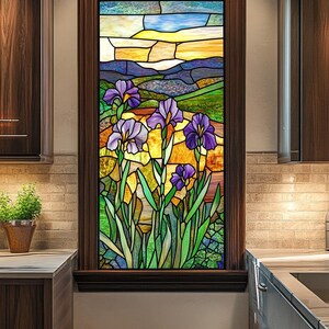 Puede incluir: Una ventana de vitrales que representa un paisaje con flores de iris moradas en primer plano y una puesta de sol sobre una cordillera en el fondo.