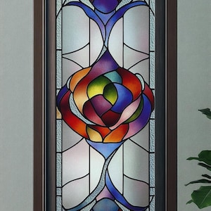 Puede incluir: Una vidriera con un diseño floral vibrante. La obra presenta una flor central multicolor en tonos de rojo, naranja, amarillo, azul y morado, enmarcada por un marco de madera marrón oscuro. El vidrio tiene una apariencia texturizada.