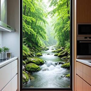 May include: A large rectangular window installed in a kitchen wall, displaying a view of a flowing river surrounded by moss-covered rocks and lush green trees. The kitchen features white cabinets on the left and wood-toned cabinets on the right.