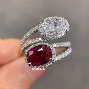 Può includere: Anello a due pietre con un diamante bianco taglio ovale e un rubino rosso. Entrambe le pietre preziose sono circondate da un alone di diamanti più piccoli, incastonati su una fascia a gambo diviso. L'anello è un gioiello di grande effetto.