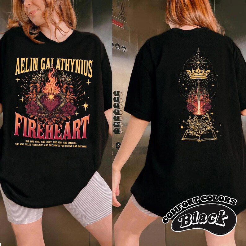Może przedstawiać: Czarny t-shirt z grafiką "AELIN GALATHYNIUS FIREHEART". Przedni wz&oacute;r przedstawia serce, płomienie i elementy kwiatowe. Tył ma koronę, miecz i wz&oacute;r książki. "COMFORT COLORS Black" jest wydrukowane w prawym dolnym rogu.