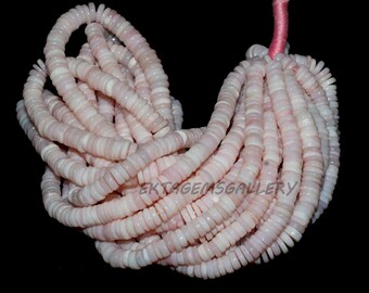 Pode incluir: Um conjunto de contas rosa claro, planas e circulares, enfiadas em um cordão rosa. As contas têm uma aparência em camadas, com uma mistura de tons rosa pálido e branco. O fundo é preto.