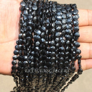 May include: Strands of black faceted gemstone beads. The beads are small, round, and have a flat, disc-like shape. The beads are strung together, creating a flowing, textured appearance. The image is well-lit, highlighting the beads' reflective surfaces. The text "Ektagemsgallery" is visible.