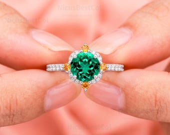 Puede incluir: Un anillo de plata con una piedra central redonda de talla brillante en color verde, rodeada por un halo de pequeñas piedras blancas y cuatro pequeñas piedras naranjas. La banda está engastada con piedras blancas y acabado pulido.
