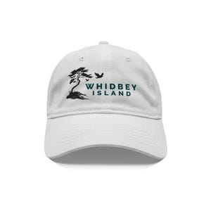 May include: White baseball cap with a curved peak. The cap displays a black graphic of a tree and birds, with the words "WHIDBEY ISLAND" in green block letters. The cap is made of a soft fabric and has an adjustable strap.