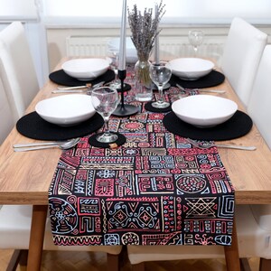 Peut inclure: Un chemin de table noir avec un motif géométrique coloré. Le chemin de table est placé sur une table en bois avec des chaises blanches et comporte des sets de table noirs et des bols blancs.