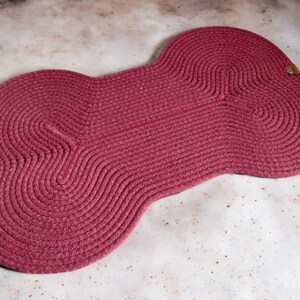 May include: A large, pink, bone-shaped rug made of woven rope. The rug has a textured surface and is perfect for adding a touch of whimsy to any room.