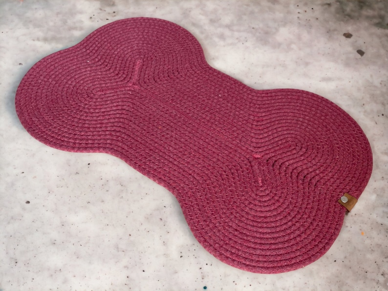 May include: A pink, woven, bone-shaped rug with a brown leather tag.
