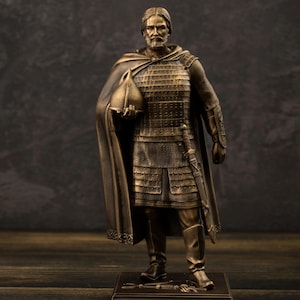 May include: A bronze-toned statue of a bearded warrior in scale armor and a cloak, holding a helmet in one hand and a sword at the hip. The figure stands on a rectangular base with the Cyrillic text "Дмитрий Донской" engraved on the front plaque.