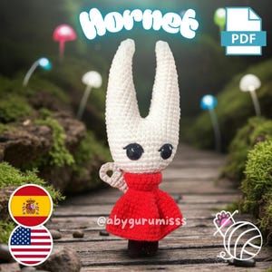 Puede incluir: Muñeca de ganchillo hecha a mano del personaje Hornet. Tiene una cabeza blanca con dos cuernos puntiagudos, ojos negros y un vestido rojo. La palabra "Hornet" está escrita en turquesa encima de la muñeca. La muñeca está sobre una superficie de madera.