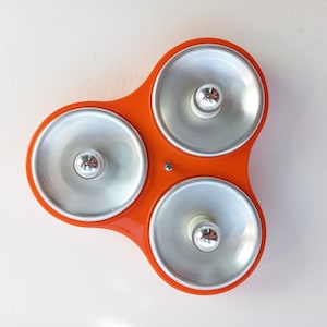 May include: Orange ceiling light fixture with three silver circular light covers. Each light cover has a small, round, silver bulb in the center.