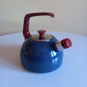 Peut inclure: Une bouilloire ronde bleu foncé pour cuisinière avec une finition brillante. Elle présente une poignée incurvée rouge foncé, un bouton rouge assorti sur le couvercle circulaire et un bec verseur argenté avec un capuchon rouge.