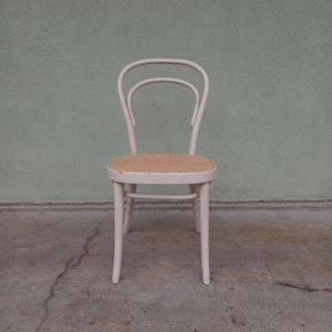 May include: White wooden chair with a woven cane seat. The chair has a curved back and a simple design.
