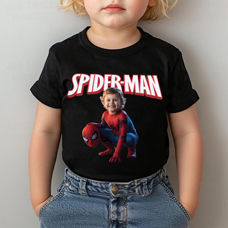 May include: Black t-shirt featuring the text "SPIDER-MAN" in white with red trim. The shirt displays a photo of a child dressed as Spider-Man. The child is wearing a red and blue Spider-Man costume and holding a Spider-Man mask.