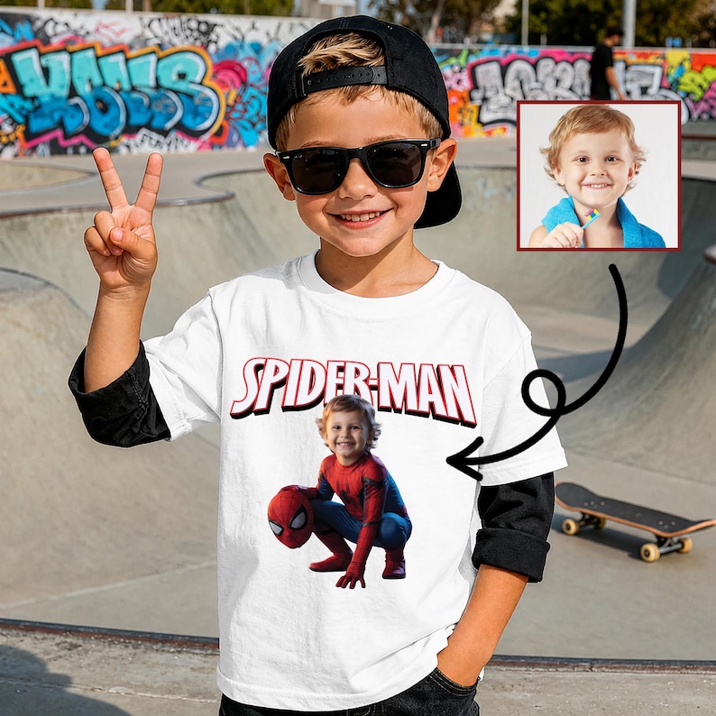 May include: A young child wearing a white Spider-Man t-shirt, black sunglasses, and a black baseball cap. The shirt features the Spider-Man logo and a picture of a child dressed as Spider-Man. The child is smiling and giving a peace sign.