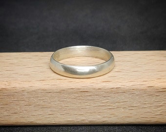 Puede incluir: Un anillo de banda de plata simple, liso y pulido, descansando sobre una superficie de madera marrón claro.