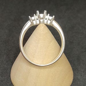 Puede incluir: Un anillo de plata con tres garras que sujetan una piedra central y dos piedras más pequeñas a cada lado.