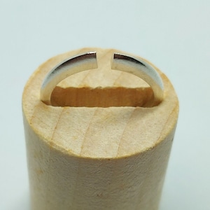 May include: A silver ring with a gap in the band, displayed on a wooden ring mandrel.