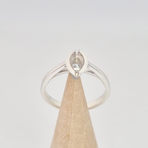 Puede incluir: Un anillo de plata con un engaste en forma de marquesa. El anillo se muestra sobre un cono de madera sobre un fondo blanco. La banda del anillo se divide en dos líneas paralelas a cada lado del engaste.
