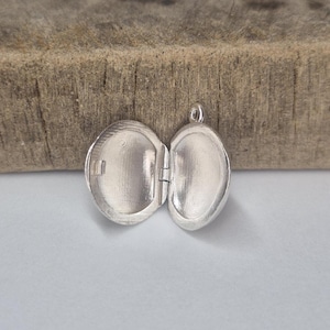 May include: A silver locket pendant with a hinged opening. The locket is oval shaped and has a smooth, polished finish.