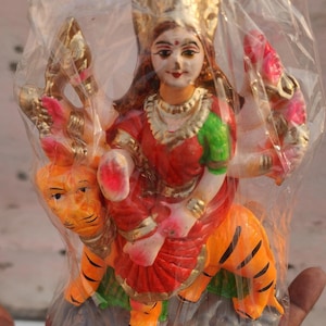 May include: A colorful figurine of a Hindu goddess riding a tiger. The goddess is wearing a red and gold dress and a crown. The tiger is orange and black with white stripes.