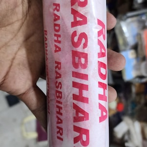 May include: A white and red package of incense sticks with the text "RADHA RASBIHARI" printed on it.
