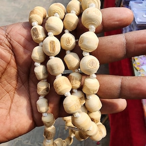 Puede incluir: Un collar de cuentas de madera de color marrón claro con un hilo blanco enhebrado. Las cuentas son redondas y tienen una textura ligeramente rugosa.