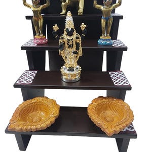 May include: A four-tiered wooden shelf with decorative details, featuring various gold and black figurines, including a deity with multiple arms, a baby deity, and two standing deities. The shelf also includes two decorative bowls.