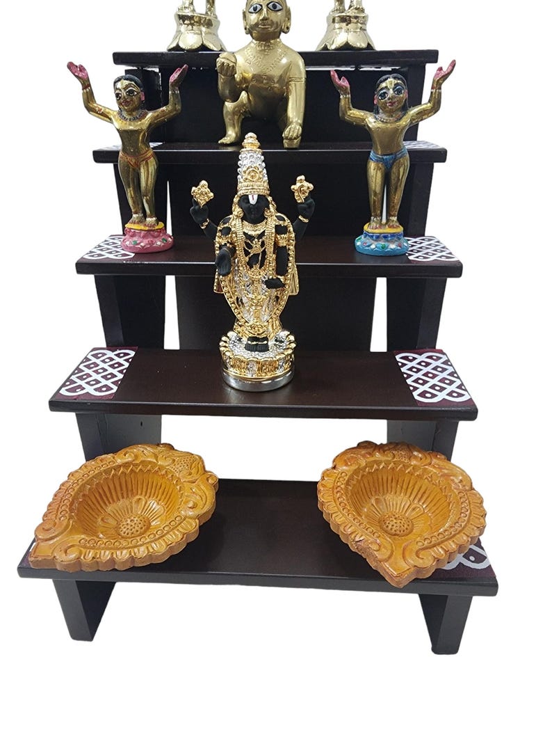 May include: A four-tiered wooden shelf with decorative details, featuring various gold and black figurines, including a deity with multiple arms, a baby deity, and two standing deities. The shelf also includes two decorative bowls.
