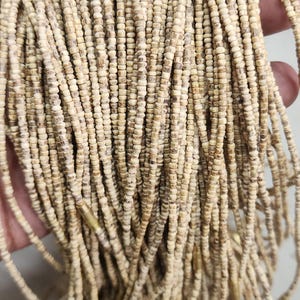 May include: A strand of natural wood beads, with a light brown color, in a close-up view. The beads are small and round, and they are strung together on a thin cord.