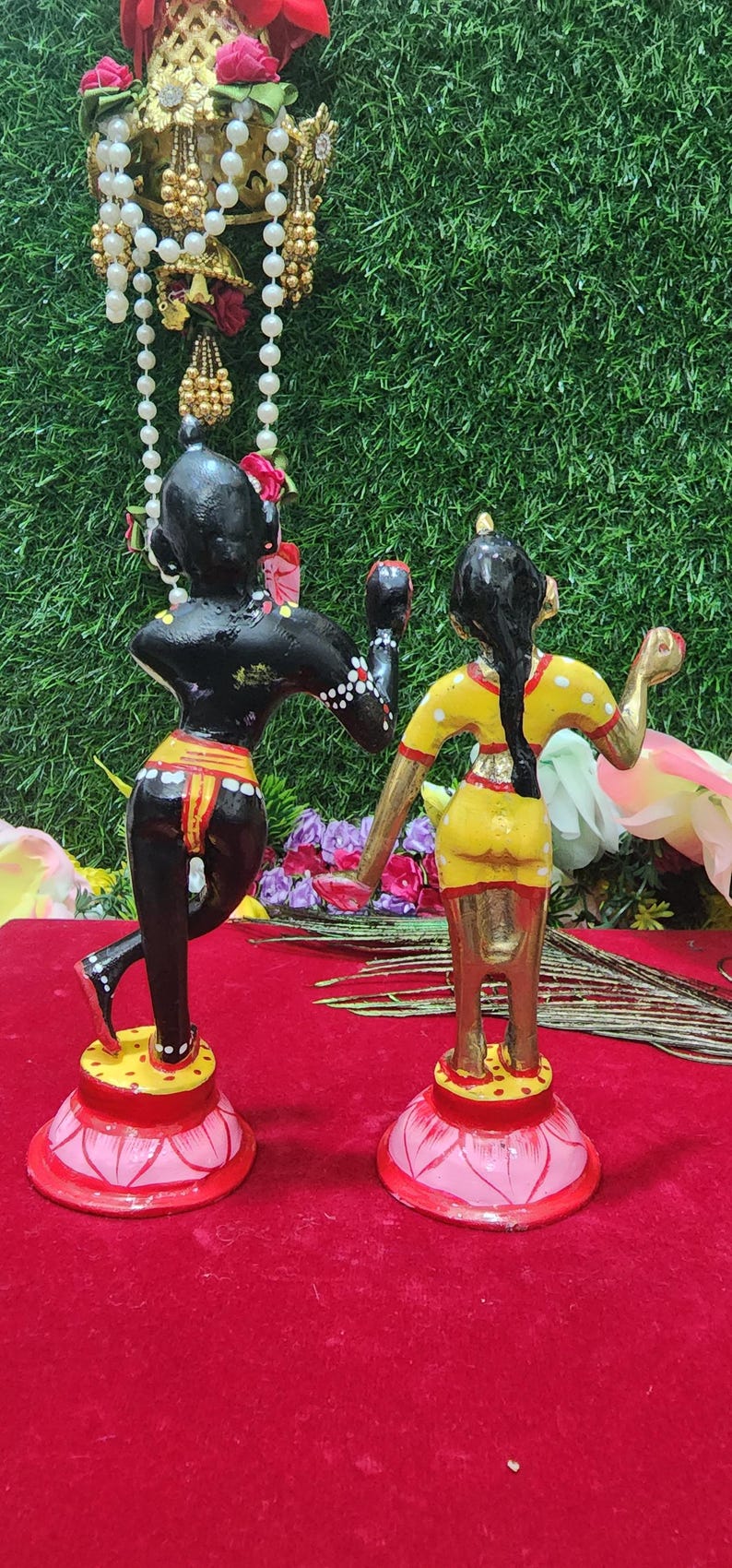 Op de afbeelding: Een paar handgeschilderde houten beeldjes die een stel in een traditionele Indiase danspose voorstellen. De mannelijke figuur is zwart met witte stippen en de vrouwelijke figuur is geel met witte stippen. Beide figuren staan op lotusvormige bases.