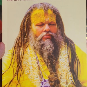 May include: A book titled "Spiritual Awakening" by Shri Hit Premanand Govind Sharan Ji Maharaj, volume 1. The cover features a man with long dreadlocks, a yellow robe, and a yellow and red mark on his forehead. The book is published by Bhajan Marg.