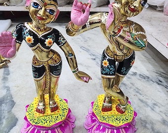 Könnte beinhalten: Zwei aufwendig bemalte Statuen von Gottheiten, eine männliche und eine weibliche, stehen auf lotusförmigen Sockeln. Die Statuen sind mit goldenen Akzenten und farbenfrohen Details verziert, darunter Blumenmuster und Pfauenfedern.